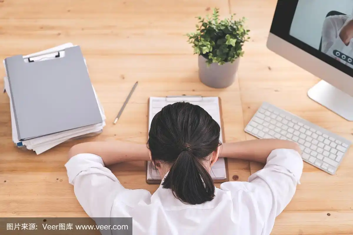 背影年轻疲惫的女商人躺在桌子上,她的脸在文件上