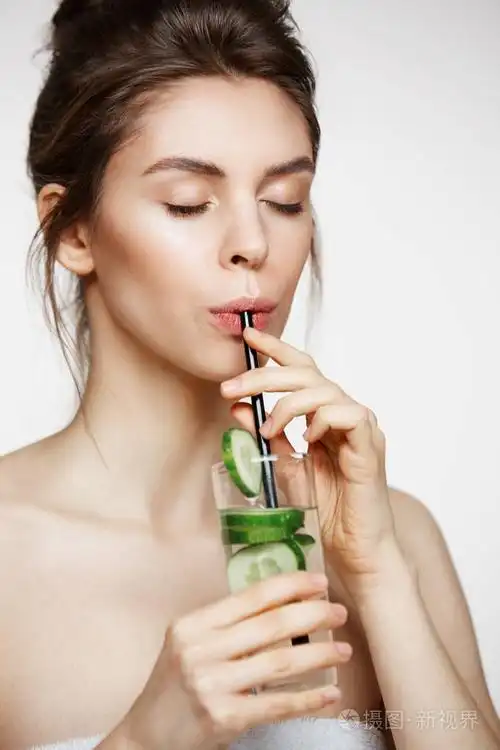 年轻漂亮的女孩在毛巾饮用水与黄瓜片在白色的背景.闭着眼睛.