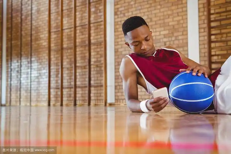 躺在球场地板上使用手机的男子篮球运动员
