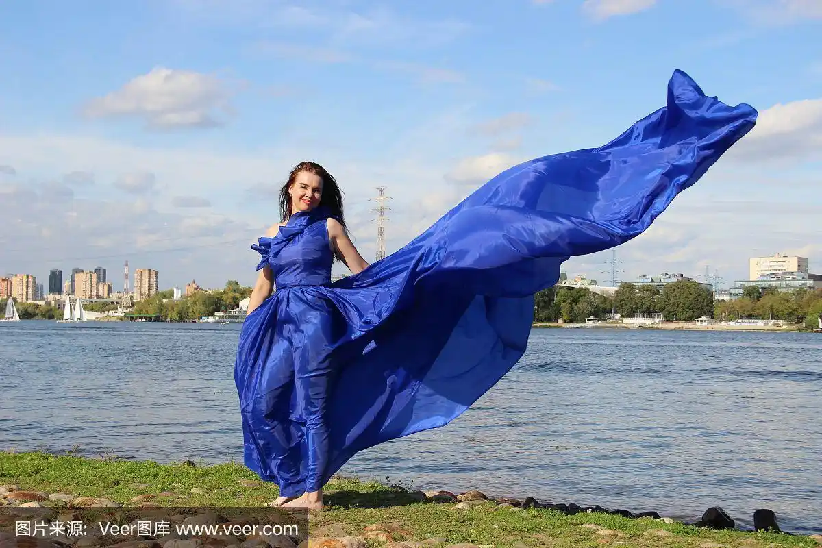 穿着在风中飘动的蓝色长裙的女人.河