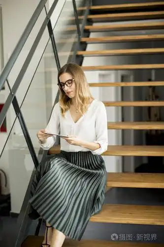 年轻迷人的女经理在现代办公室的楼梯上工作的数字平板电脑照片-正版