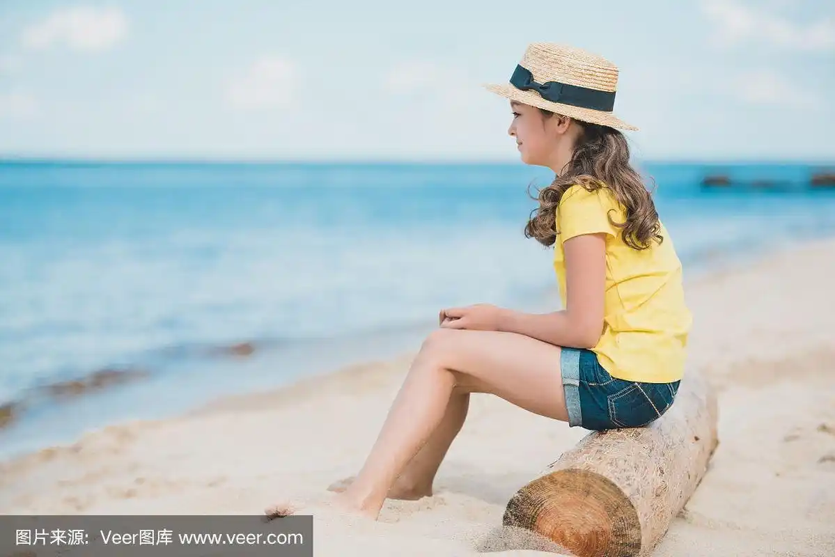 可爱的小女孩坐在沙滩上的木箱上的侧视图