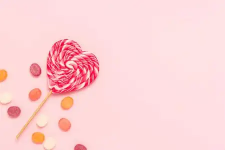 心形棒棒糖和五颜六色的糖果在柔和的粉红色背景上.糖果的概念.