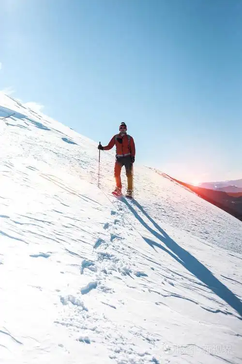 一个人爬上山顶.登山运动员在雪地鞋背着一个背包.在冬天的山上旅行.