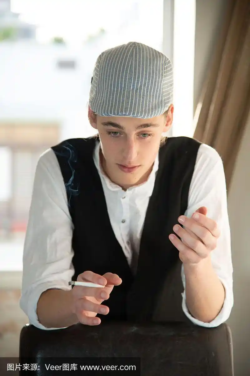 一个头戴便帽,身穿背心的年轻人在窗边抽烟.以色列
