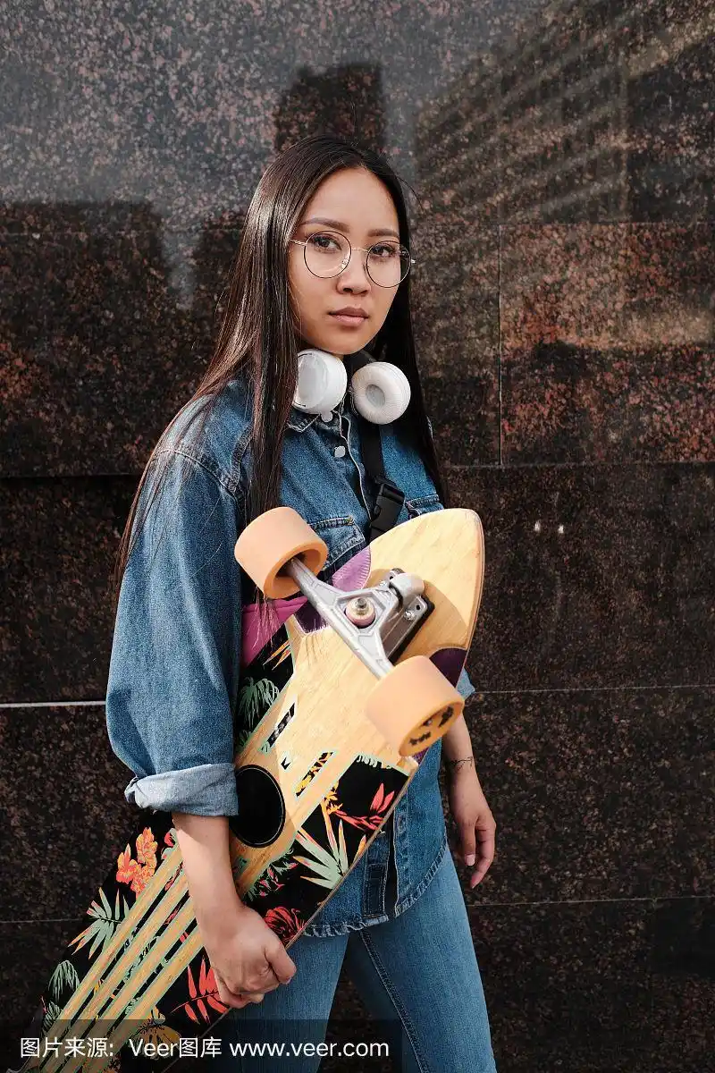 女孩拿着长板在大理石墙边摆姿势.
