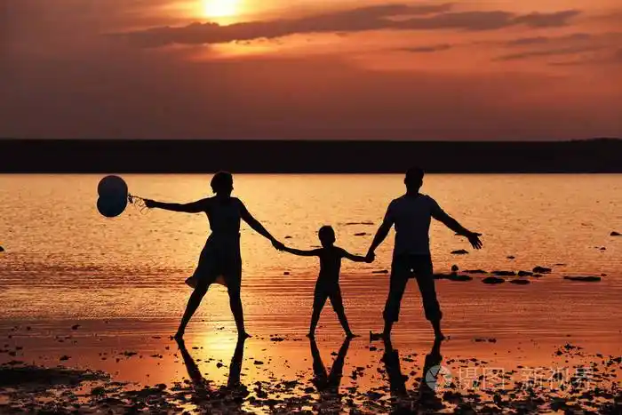 日落时湖岸上一家人的剪影. 爸爸妈妈和宝宝牵着手. 暑假休息.