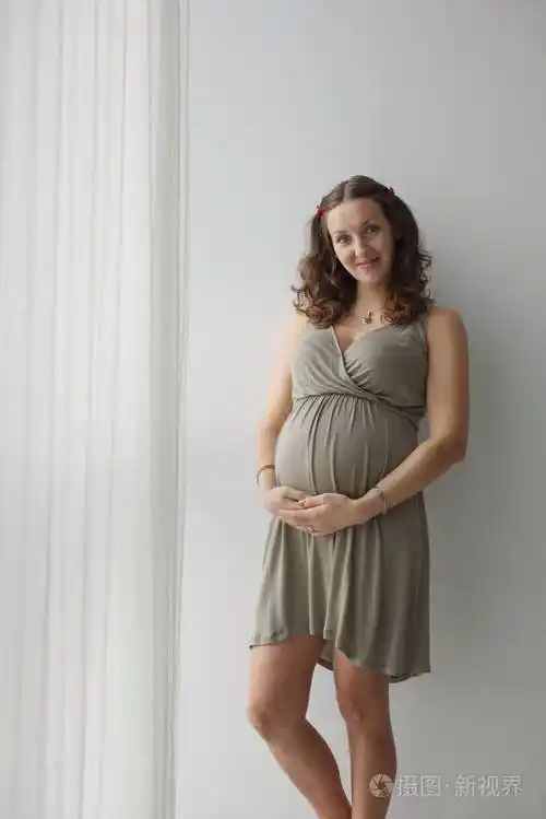 照片中幸福的孕妇抚摸着她的大肚子看着镜头微笑着在等孩子做母亲