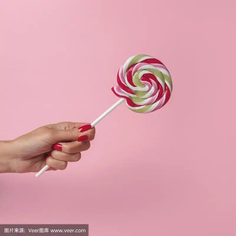 在粉红色的背景上,女人手拿着五颜六色的旋涡棒棒糖.夏季最小的概念.