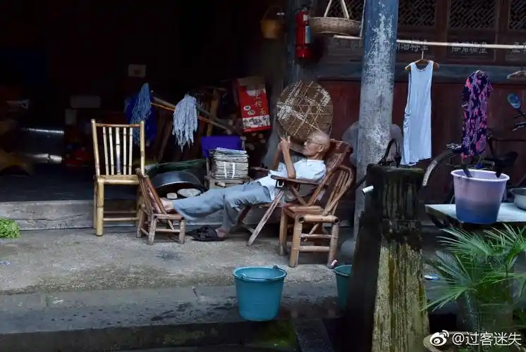 老人悠闲的躺在老藤椅上,摆弄着现代化智能机手机