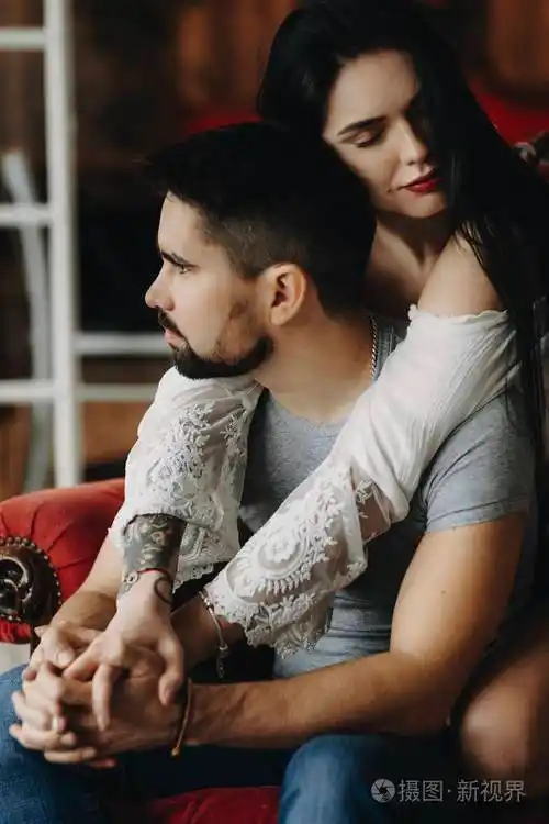 坐在一张红色的椅子上,有纹身和红唇的女孩正从背后拥抱着他的男人