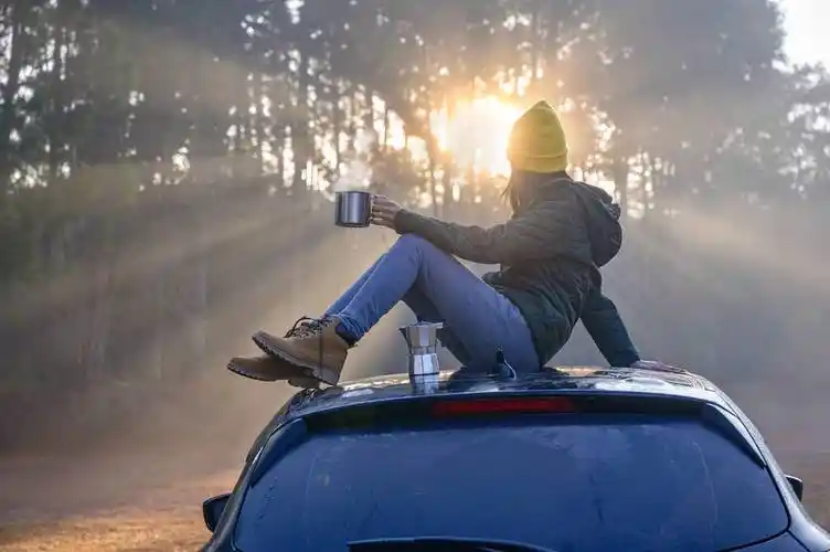 女旅行者在自己的车顶上享受着喝.