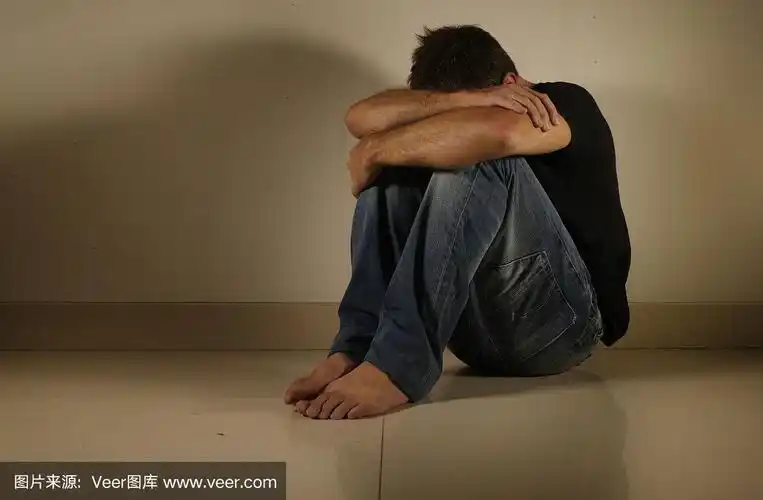 年轻绝望和抑郁的男人独自哭泣坐在家里地板在阴暗和戏剧工作室的光线