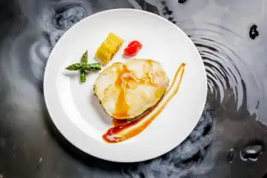 白色圆瓷盘装的香煎银鳕鱼摆放在干冰缭绕的水中