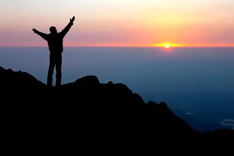 日出时站在山顶上的男人拥抱太阳