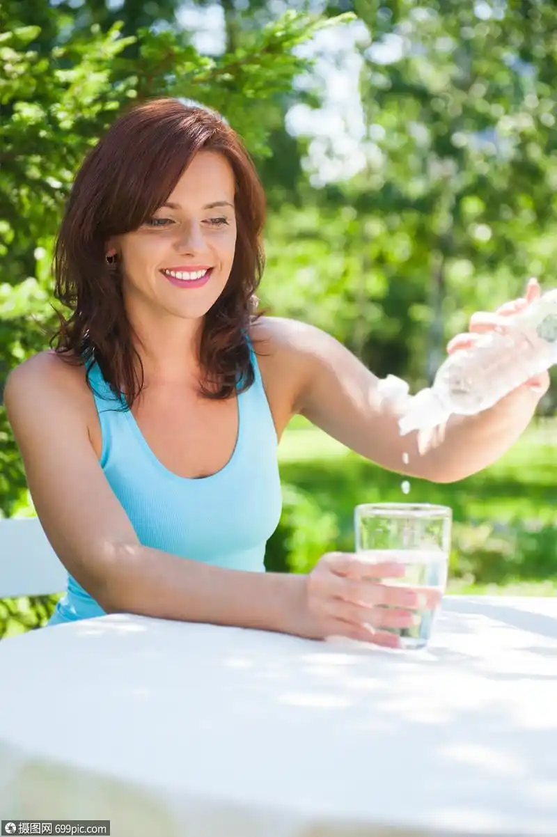 轻美丽的女人夏季绿色公园野餐时喝水的肖像
