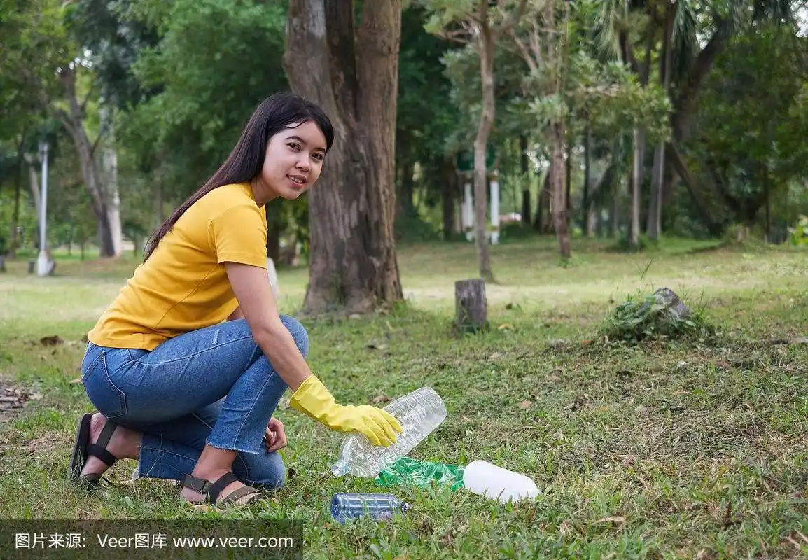 穿着黄色t恤的年轻女子在公园里捡垃圾.在公园做志愿者.