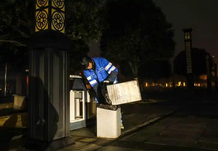 清晨,清洁工张兴中在都梁广场清理垃圾桶内的垃圾.(摄影:熊伟)