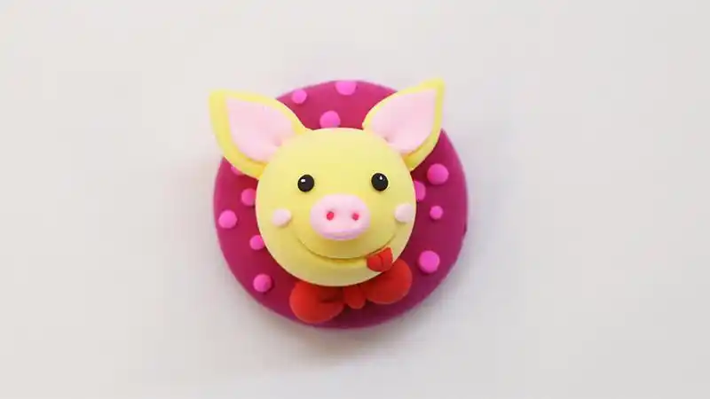 1,首先取一团浅黄色的粘土,搓成圆形,作为小猪的脑袋,上面粘一块粉色