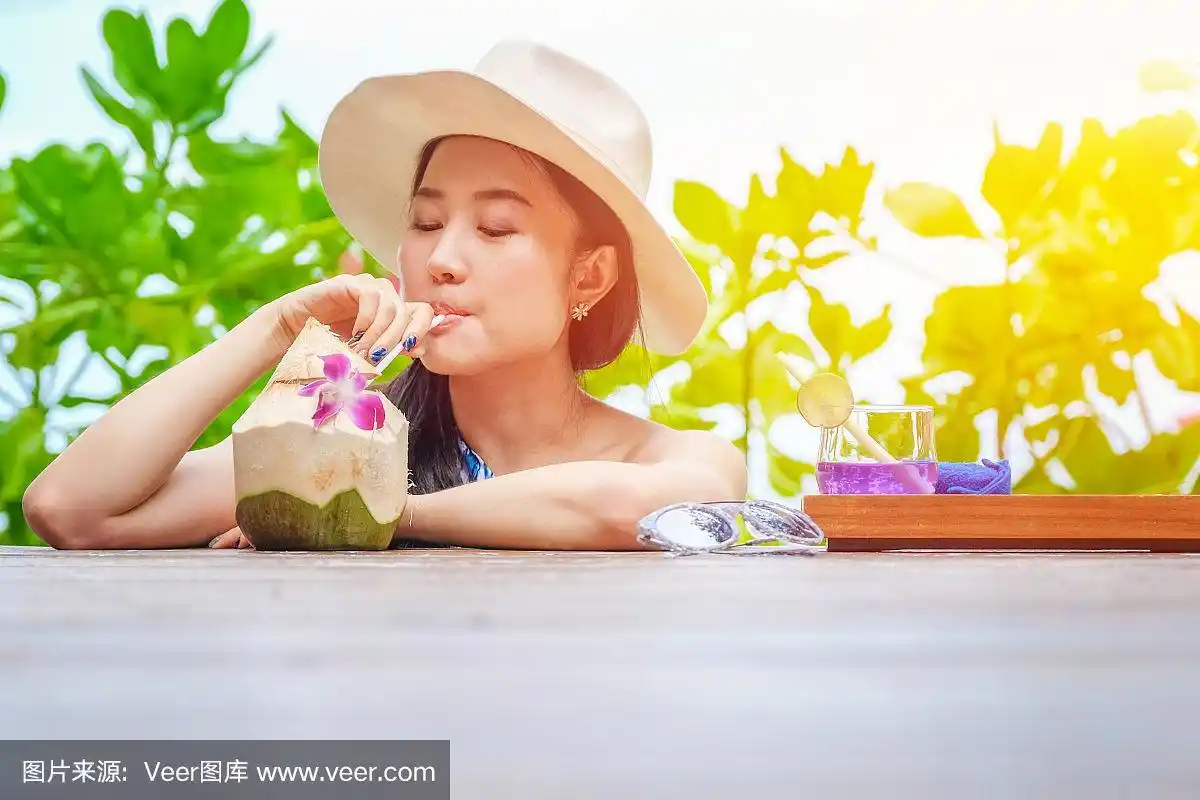 快乐的女人在沙滩上喝着新鲜的椰子汁