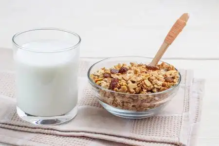 一杯牛奶和牛奶什锦早餐在玻璃器皿和木勺照片