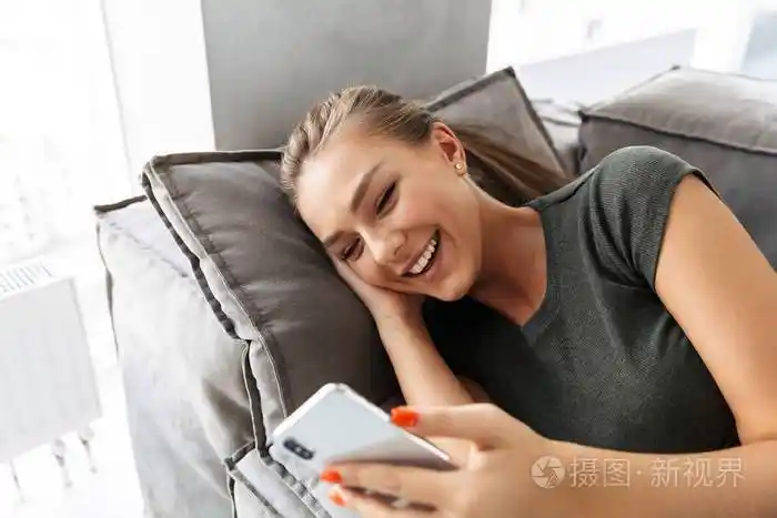 快乐的年轻女人在家里躺在沙发上用手机