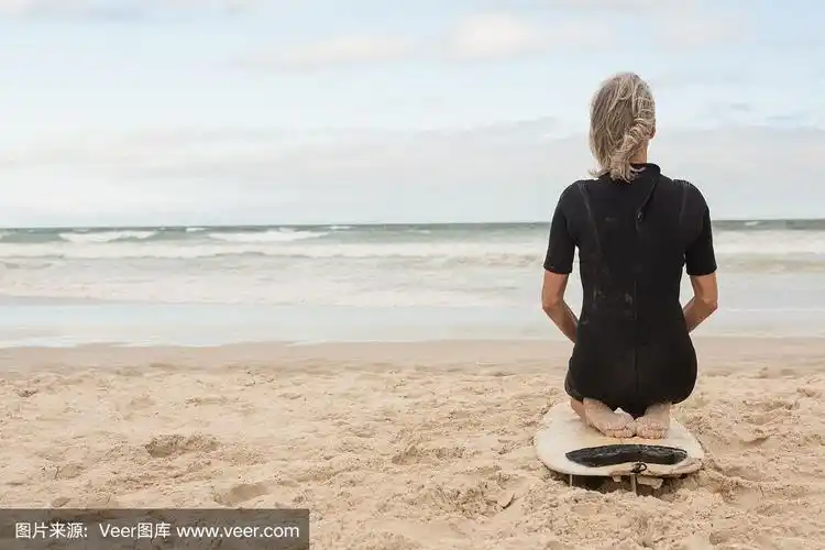 后视图的女人跪在冲浪板上反对多云的天空