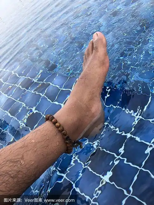 亚洲印度男子的脚和脚踝在游泳池里,赤裸的湿毛腿照片与木珠脚踝手镯