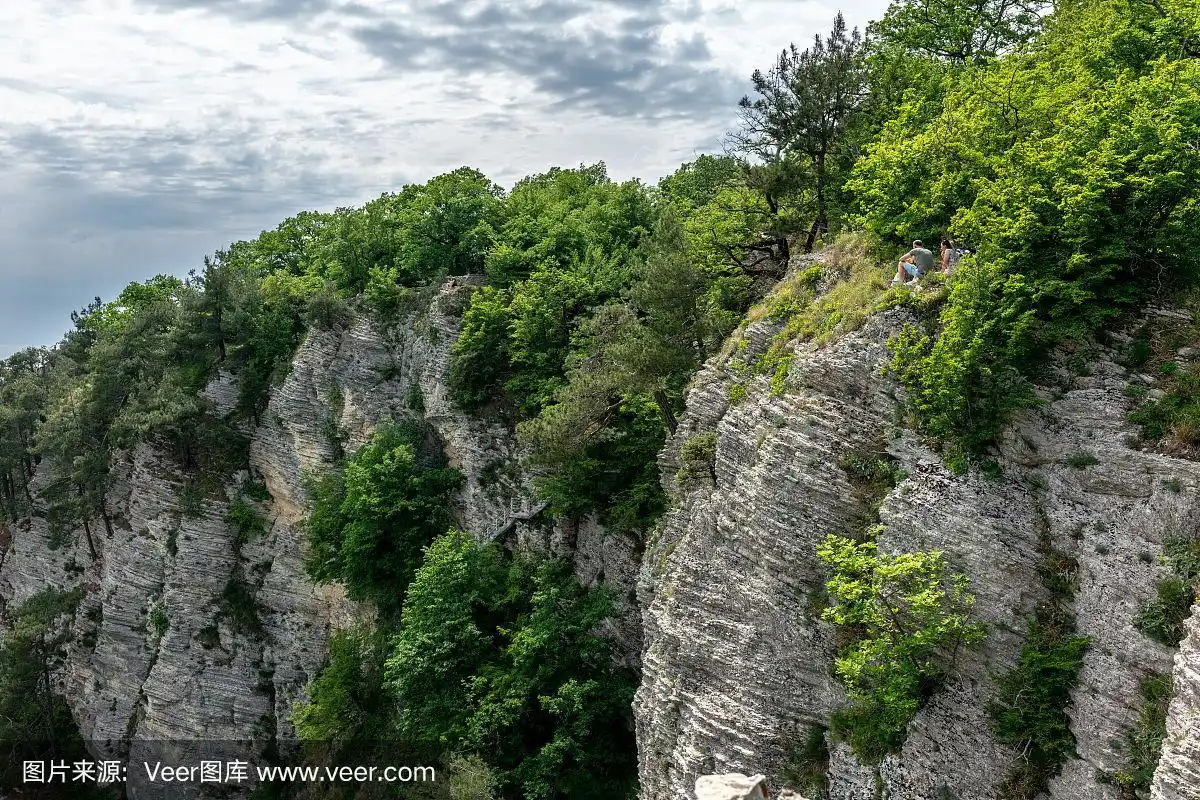 有陡峭岩石斜坡的山.有几个人坐在悬崖上.