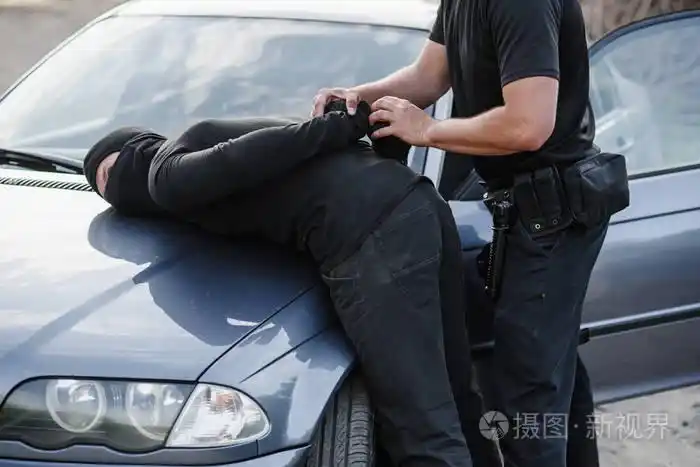 一名警官用一辆偷来的汽车的面具逮捕了罪犯, 并把他铐在车盖上.