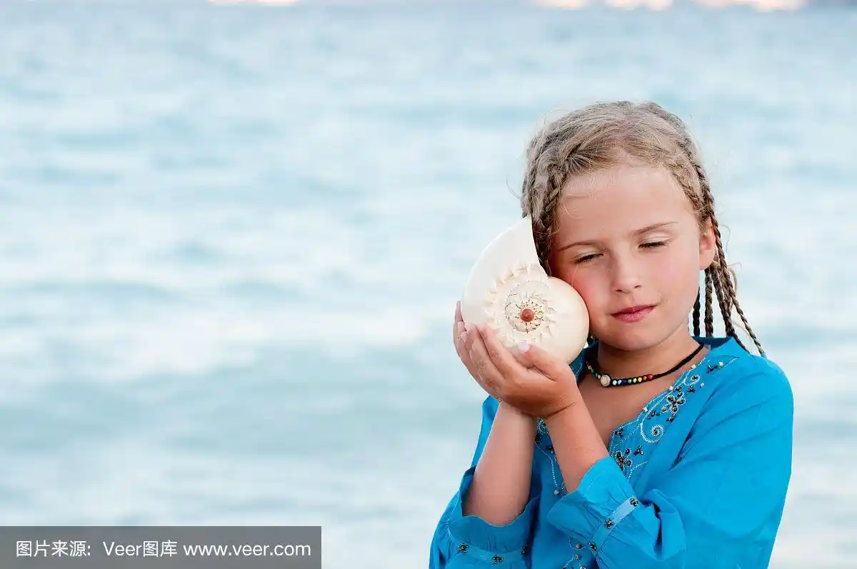 年轻的女孩拿着海螺壳听着大海的声音