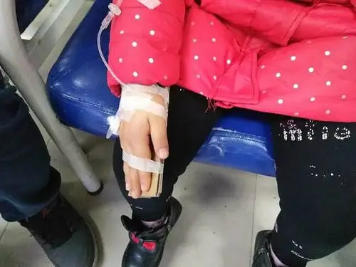 孩子输液时,打着针的小手被胶带粘在一个长方形的硬纸板上,这样固定住