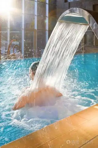 英俊的男人在游泳池放松,淋浴按摩水疗,在豪华酒店与大玻璃窗,自然