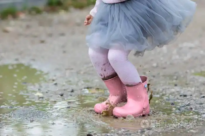 当她在雨中跳跃和玩耍时,水从孩子的脚上溅落.