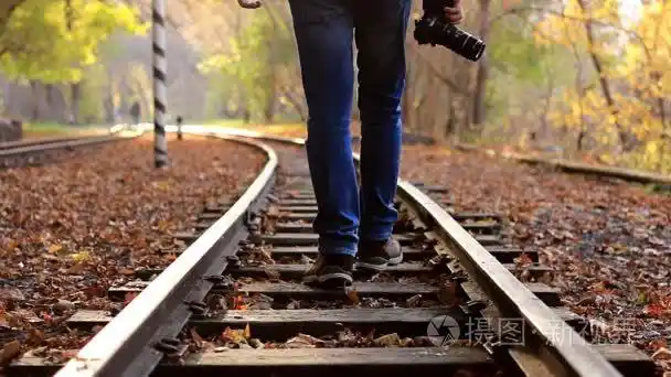 一个带着单反相机的人在一个背景的秋天森林里走下铁轨一个人从镜头前