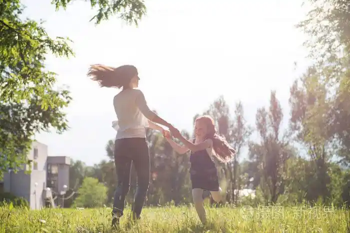 妈妈和女儿手牵手在草坪上旋转