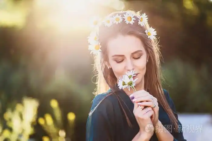 微笑的女孩与雏菊花环在她的头上持有甘菊背光