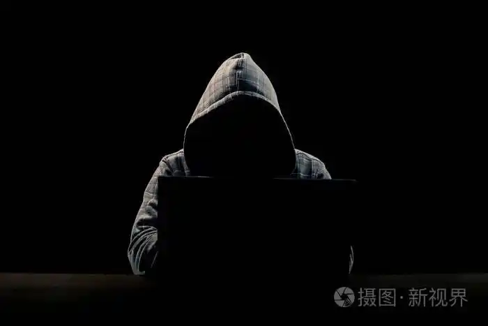 一个男人的剪影在一个黑色的背景罩, 他的脸是不可见的, 他坐在电脑.