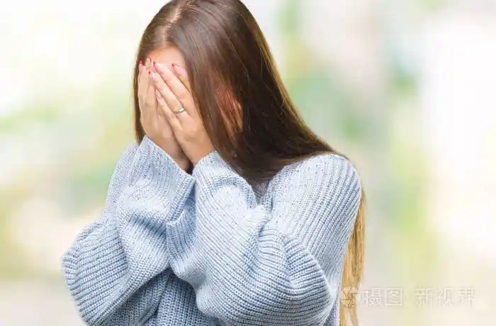 年轻美丽的白人妇女穿着冬季毛衣在孤立的背景与悲伤的表情覆盖脸与手