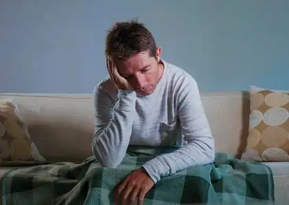 年轻的悲伤和绝望的男人坐在客厅沙发上,沮丧和压力,担心问题,感到