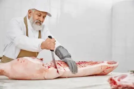 穿着制服的老屠夫用刀切猪肉.照片
