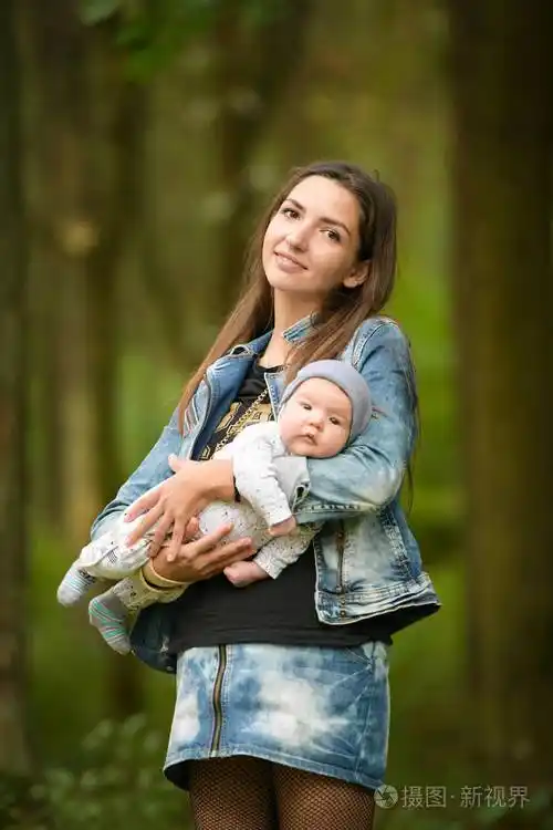 在春天的小巷里,一个微笑的年轻妈妈手上抱着一个婴儿.