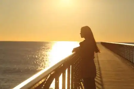 日落时分,一个女人独自从一座桥上眺望大海照片