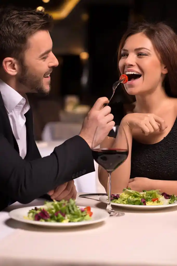 夫妇互相喂食,真好吃 !美丽的年轻夫妇互相喂食和花时间在餐厅,微笑着