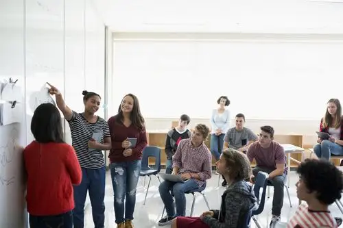 high school students giving presentation whiteboard in classroom