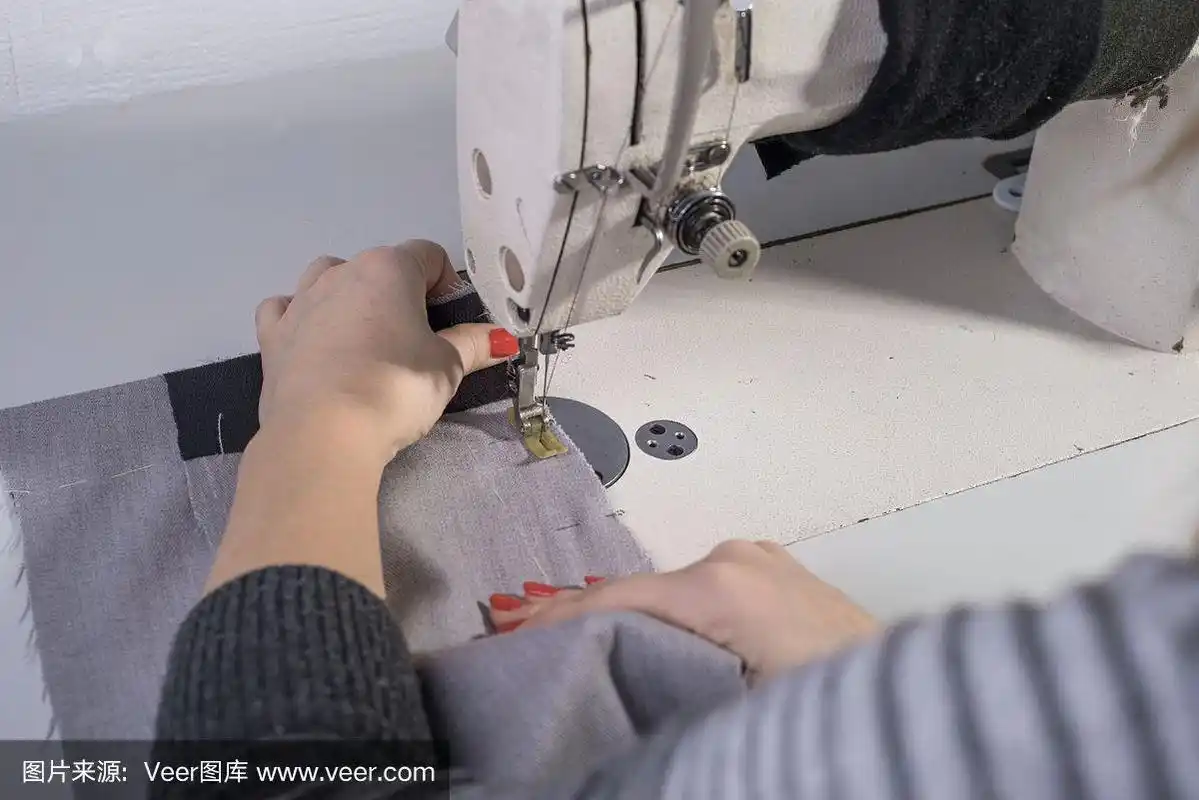 一个女裁缝缝纫衣服的手的特写,在缝纫机后面缝织物