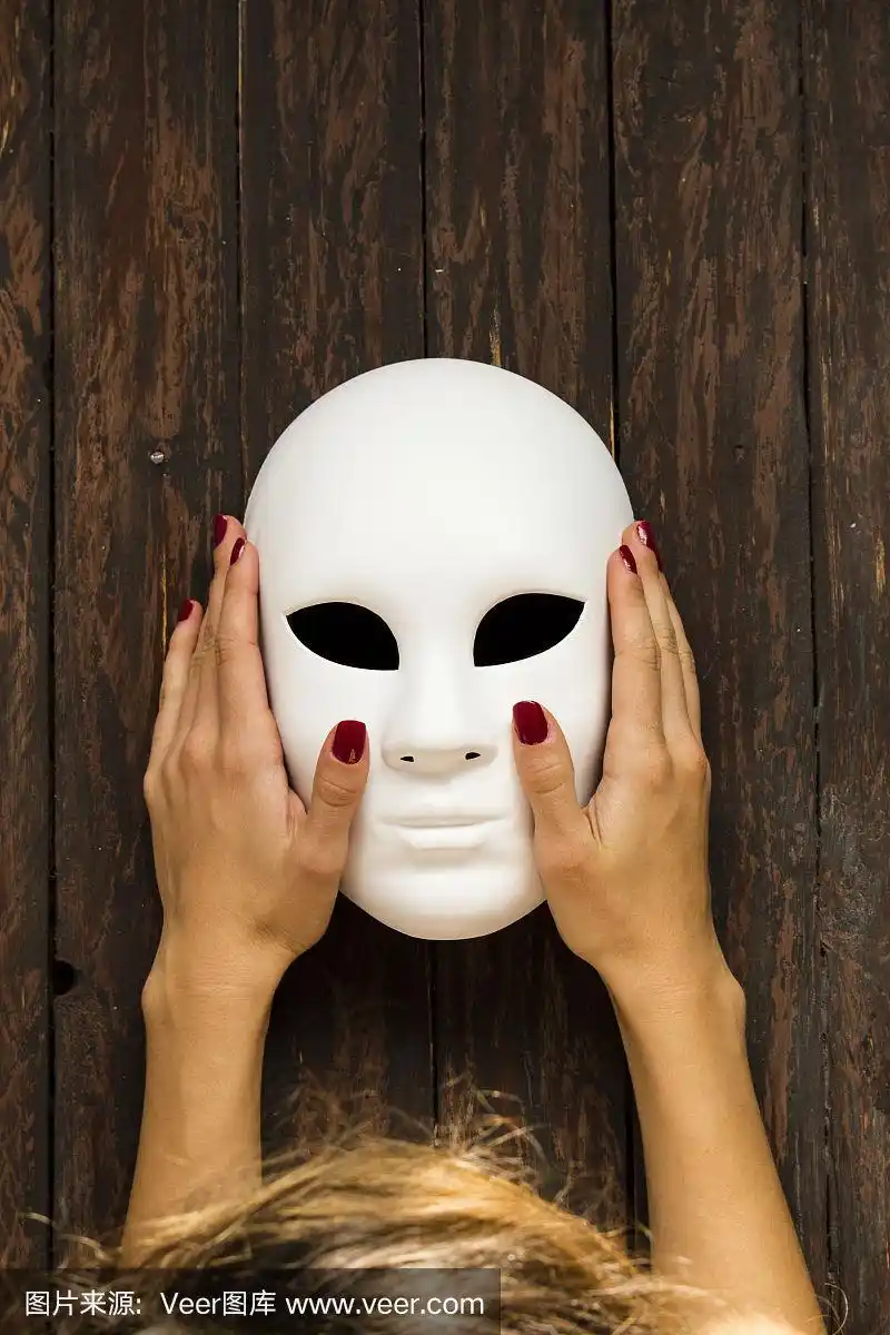 女人的手拿着白色的面具在木制的背景