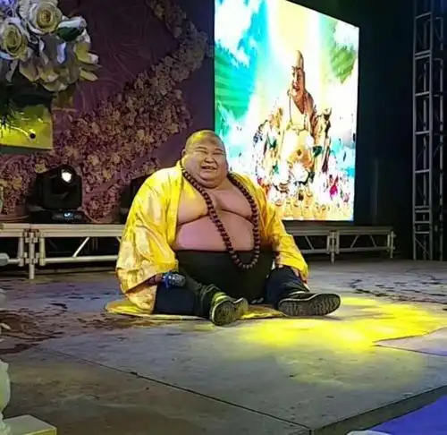 真人版"弥勒佛",表演坐着笑,观众看到后,纷纷朝其扔钱讨吉利