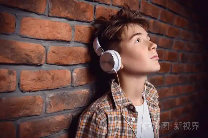 一个年轻男孩的肖像,戴着耳机,穿着休闲服,摆在砖墙上.