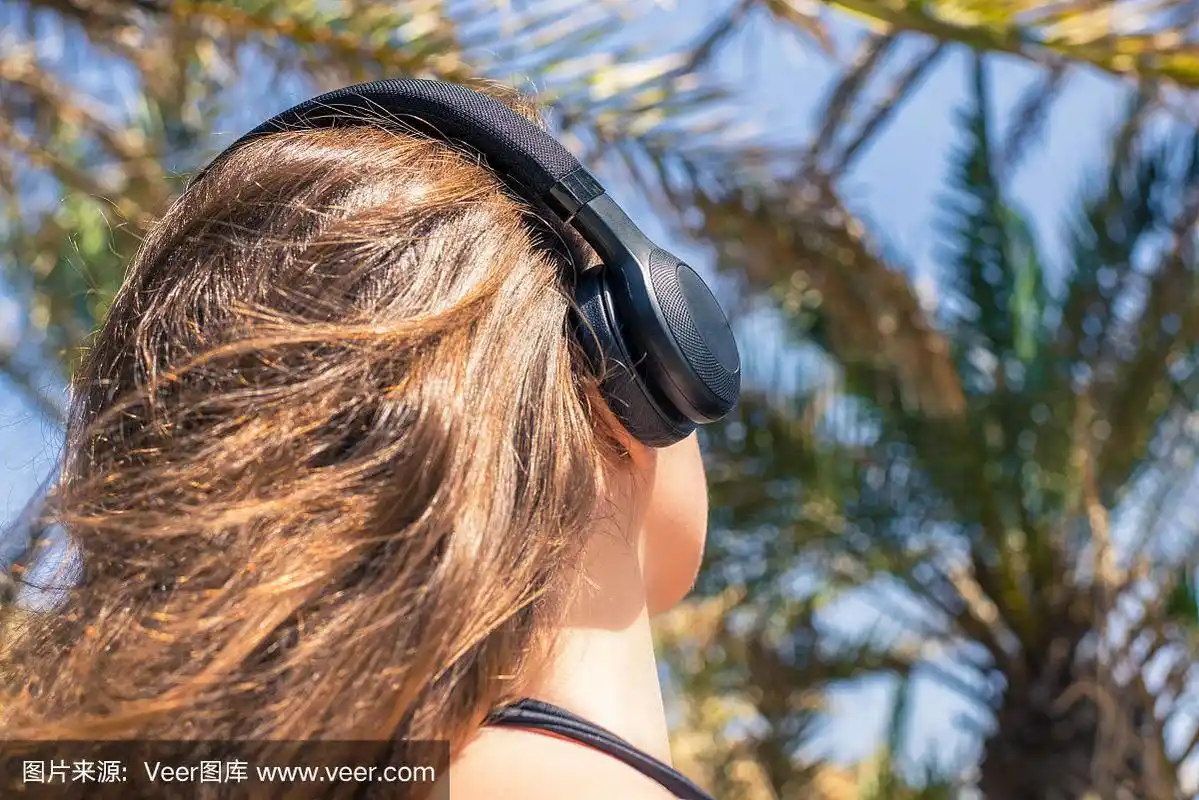 背影上的女孩戴着耳机听着音乐走在棕榈树林中.塞舌尔群岛